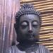Buddha-Kopf mit Stirnmal vor einer Wand aus Holz und Bambus