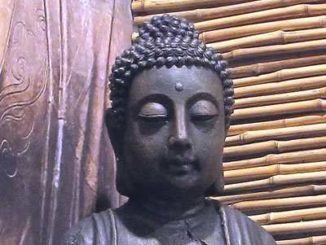 Buddha-Kopf mit Stirnmal vor einer Wand aus Holz und Bambus