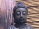 Buddha-Kopf mit Stirnmal vor einer Wand aus Holz und Bambus