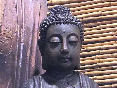 Buddha-Kopf mit Stirnmal vor einer Wand aus Holz und Bambus