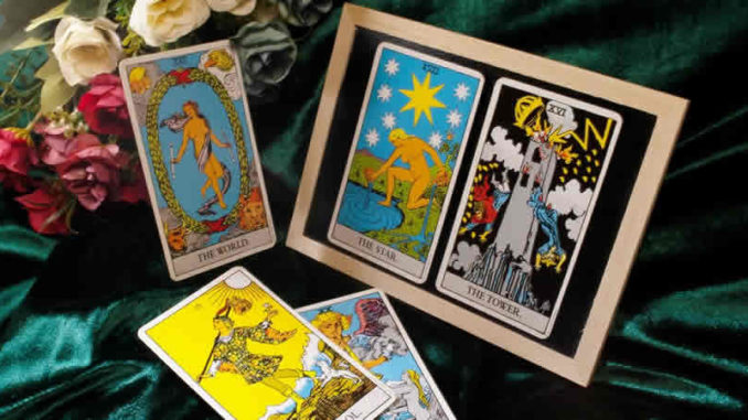 Tarotkarten mit Welt, Stern, Turm und Narr auf grünem Stoff neben Rosen