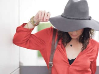 Frau in roter Bluse mit gesenktem Kopf und grauem Hut