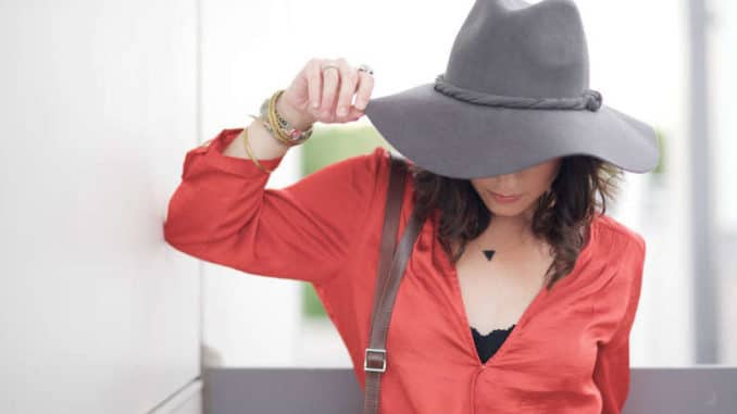 Frau in roter Bluse mit gesenktem Kopf und grauem Hut