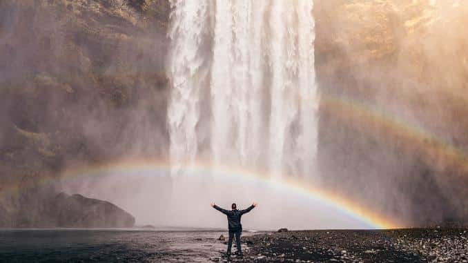 Mann am Wasserfall unter einem Regenbogen