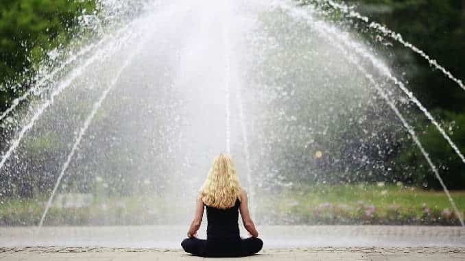 Frau meditiert vor einem Springbrunnen – Symbolbild für bewusste achtsame Ernährung