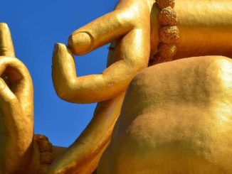 Mudras an einer goldfarbenen Buddha-Statue vor blauem Himmel