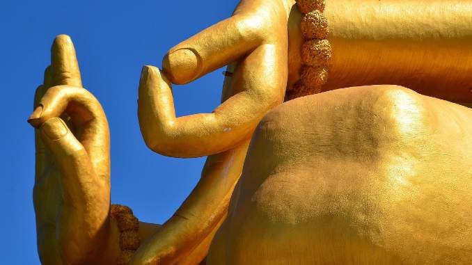 Mudras an einer goldfarbenen Buddha-Statue vor blauem Himmel