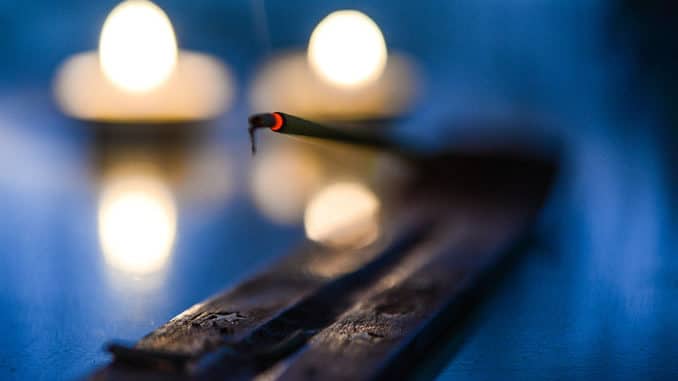 Glühendes Räucherstäbchen vor unscharfen Kerzenlichtern