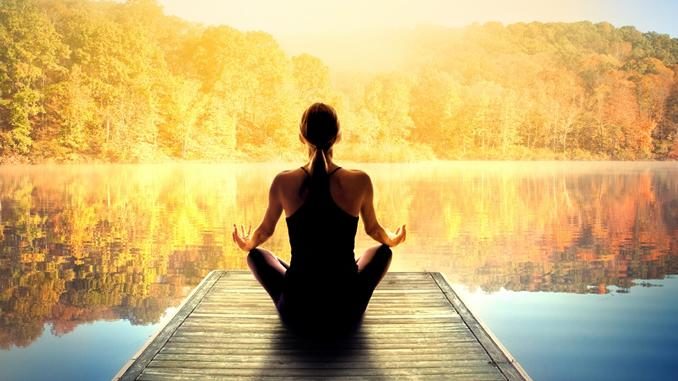 Meditation am See als Symbol für Licht und Ruhe Symbolbild zur Lichttherapie: Frau meditiert auf einem Holzsteg vor einem See im Sonnenlicht